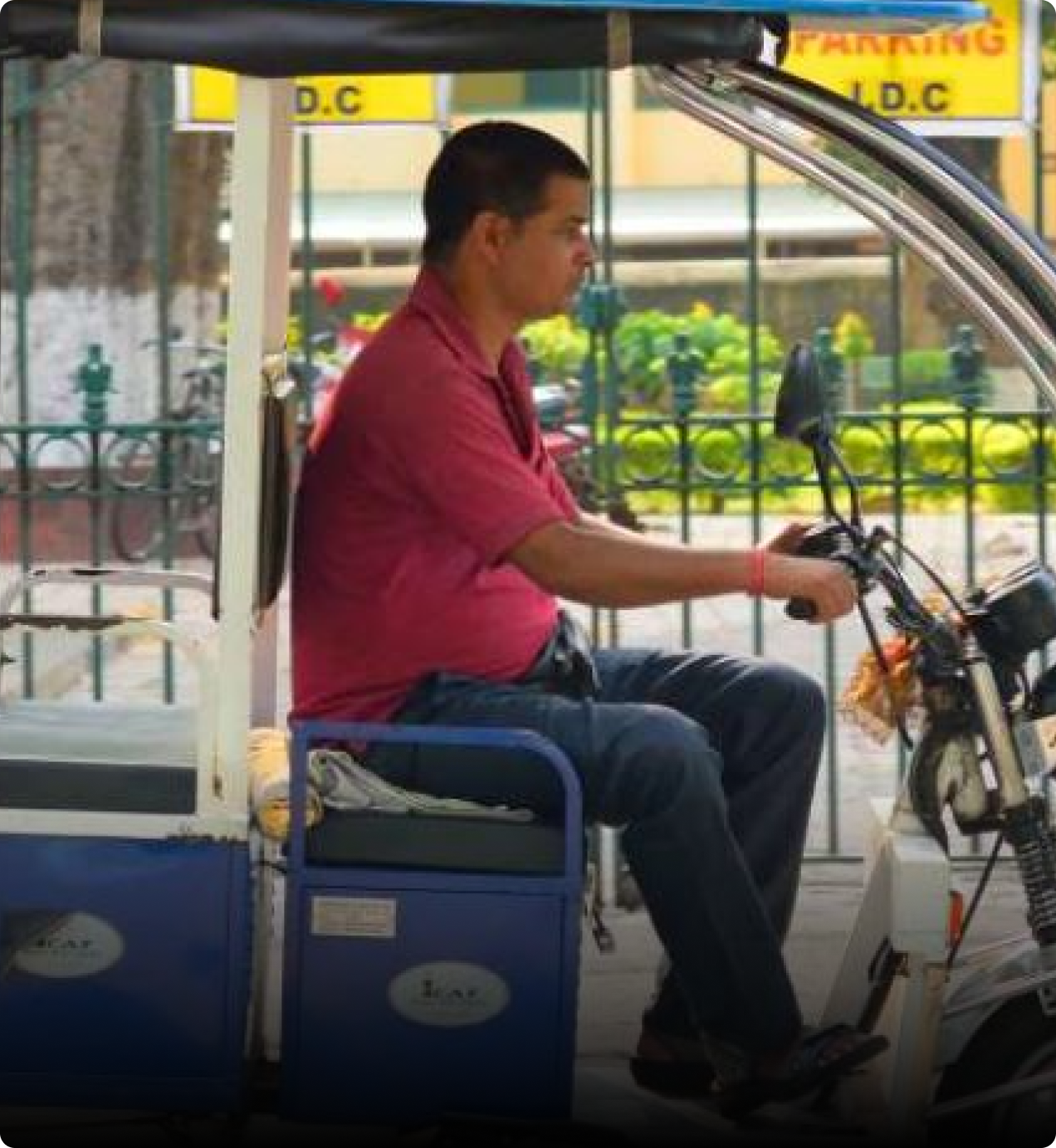 Man in a red shirt driving a blue electric rickshaw on a city street.